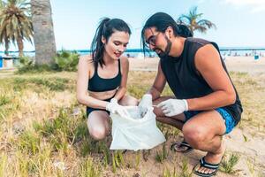 A man and a woman are picking up trash and putting it in a plastic bag on the beach photo