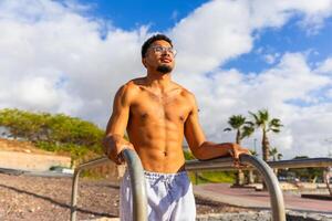 A man with a beard and glasses stands between bars during a workout photo