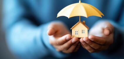 Hands holding small house under yellow umbrella, symbolizing protection and security. creative representation of home safety photo