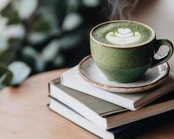 steaming matcha latte in green cup sits atop stack of books, creating cozy atmosphere photo