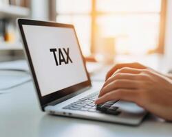 Hands typing on laptop with TAX displayed on screen, symbolizing tax filing and financial management photo