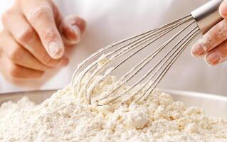 Mixing flour into batter with whisk, close up of hands and ingredients photo