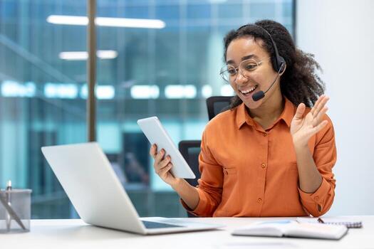Office worker using smartphone and laptop with headset in modern workspace, engaging in online meeting, multitasking across devices, showcasing professional communication skills and remote work setup photo