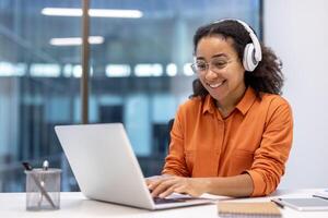 Female programmer wearing headphones, coding new software on laptop. Focused and happy while working in modern office. Ideal for technology, business concepts, inspiration. photo