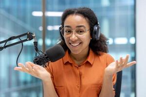 Woman confidently hosting podcast, wearing headphones, speaking into microphone. Gestures add dynamic energy, capturing mood of discussion. Perfect for themes of podcasting and communication. photo