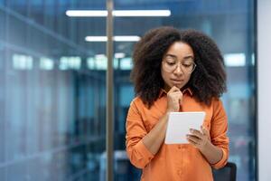 Confident woman in office contemplates information on digital tablet, demonstrating focus and professionalism. Calm setting highlights analysis, business potential, and technology use. photo