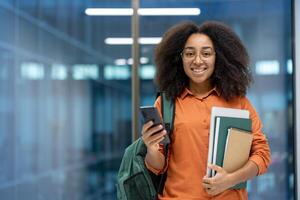 A confident student with books, and a hone standing in a bright university hallway. Portraying determination and positivity, emphasizing education and technology in a modern academic environment. photo