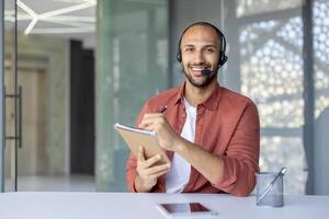 Webcam view, a man with a headset and a notepad in his hands looks into the camera, records data while listening to an online meeting and conference with colleagues and partners. photo