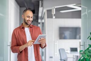 Successful satisfied businessman using tablet computer inside office at workplace, man in casual shirt reading online report, programmer developer testing new software. photo