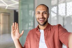 Joyful man looking into phone camera, talking to colleagues and partners remotely using call, office worker at workplace inside office. photo