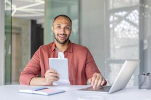 Portrait of a young successful businessman at the workplace, man looking at the camera with a tablet computer in his hands, office worker using a laptop at work. photo