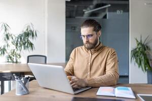 Focused professional using a laptop at a desk in modern office. Concept of productivity, business, and technology usage in a professional workspace. photo