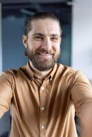 A cheerful individual in casual attire capturing a selfie in an office, emphasizing friendly and approachable professionalism. photo