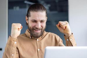 A man in a professional setting is enthusiastically celebrating a personal or professional success. He is expressing joy and victory through his emotions and body language. photo