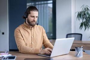 A business professional wearing a headset works attentively on a laptop in a modern office setting, showcasing remote work and communication in a corporate environment. photo