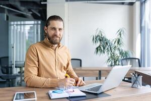 A confident professional sitting at a desk in a bright office, focusing on work using technology and writing tools. The image captures a productive and modern business environment. photo