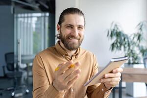 Person with beard wearing casual attire enthusiastically taking notes in a professional office setting, suggesting collaboration. photo