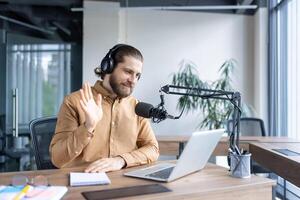 Man in an office using professional audio equipment and a laptop, engaging with an online audience through thoughtful communication and a casual demeanor, emphasizing content creation photo