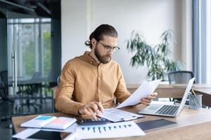 A focused business professional working at their desk, analyzing documents and data with precision in a modern office environment. photo