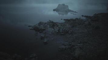 Calm waters reflect distant island in twilight atmosphere over rocky shore video
