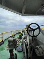A ship's wheel frames a breathtaking seascape under a tranquil sky. Yellow deck fittings and a calm ocean create a peaceful, maritime scene photo
