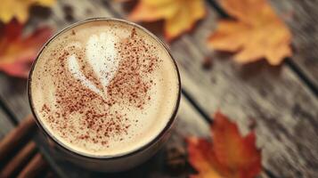 Autumnal latte art in glass, cinnamon, fall leaves on wood. photo