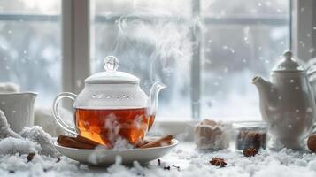 Steaming tea in glass teapot on snowy windowsill. photo
