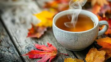 Steaming cup of tea surrounded by autumn leaves on rustic wood. photo