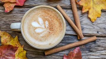 Autumnal latte art in a ceramic mug, surrounded by cinnamon sticks and fall leaves on a rustic wooden surface. photo