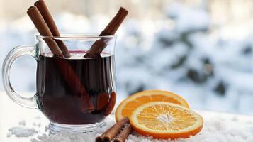 Warm mulled wine in glass mug with cinnamon sticks and orange slices on snowy surface. photo