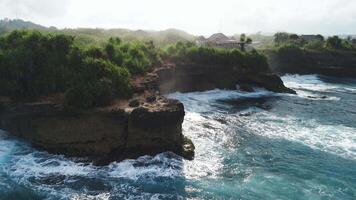 Rocky coastline with crashing ocean waves and sunshine with fog on Nusa Lembongan, drone view video