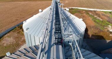 Modern granary in a sunny daytime. Metal construction on the top of grain elevator on field background. Top aerial view. video