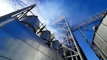 Huge hangar premises. Grain elevators outdoors. White vapor released from metal granary for drying grains. Close-up. View from below. video