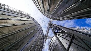 Modern grain terminal. Metal storage tanks for drying grain. Industrial equipment for agribusiness. Large grain elevators on blue sky background. Close-up. video