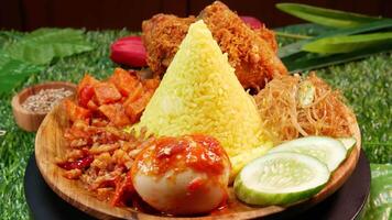 An Indonesian specialty dish of cone-shaped yellow rice, crispy fried chicken, fried vermicelli, sambal egg, cucumber slices, and fresh red sambal. video