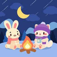 Cute winter camping illustration of a bunny and cat sitting by a campfire under the moonlight, enjoying hot drinks in a snowy mountain setting. vector