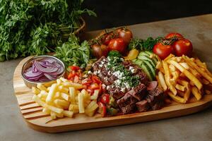 A wooden tray with a steak, french fries, and vegetables photo