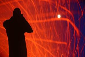 Silhoette of photographer with trails of sparks in front of sky with bright moon photo