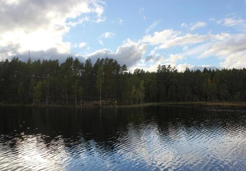 Lake in front of a forest and clouds in Varmland, Sweden. The water displays mirror-like reflections. photo