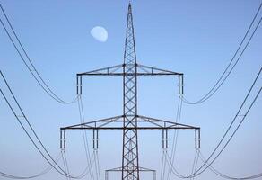 Symmetrical view on a high voltage power line. The moon is visible in the background. photo