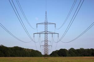 Symmetrical view on a high voltage power line on a rural landscape with forest to both sides. The moon is visible in the background. photo