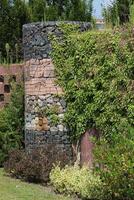 Wall with differently shaped stones in metal mesh. It is partly overgrown. photo