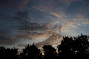 Different impressive and colorful clouds in the morning with some tree silhouettes photo