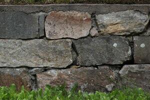 Old fashioned stone wall with grass on the ground. photo