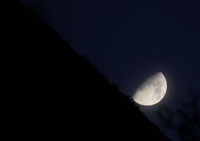 Partial moon on dark blue with slightly visible horizon in unusal angle. photo