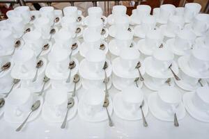 A row of elegant white cups with matching saucers and finely crafted spoons on a wellset table creates an inviting dining aesthetic, enticing guests to enjoy a delightful meal photo