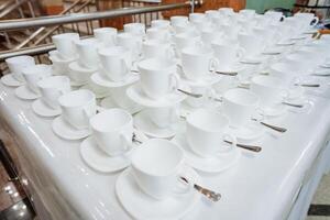 On the table, there is a neatly arranged row of white coffee cups sitting alongside their matching saucers, creating an inviting atmosphere for coffee lovers to enjoy a warm beverage photo