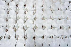 A neatly stacked collection of white cups and silver spoons presents an organized, appealing arrangement of kitchen essentials, balancing simplicity with elegance and cleanliness photo