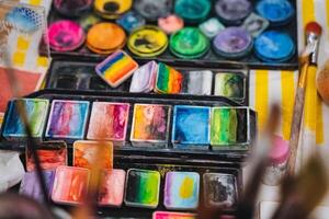 On a table, there lies a beautiful palette filled with vibrant watercolors, alongside various brushes ready for use, inviting creativity and artistic expression in watercolor painting photo
