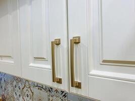 This is a close up view of a beautifully designed kitchen cabinet featuring elegant gold handles that add a touch of sophistication and style to the overall decor of the kitchen photo
